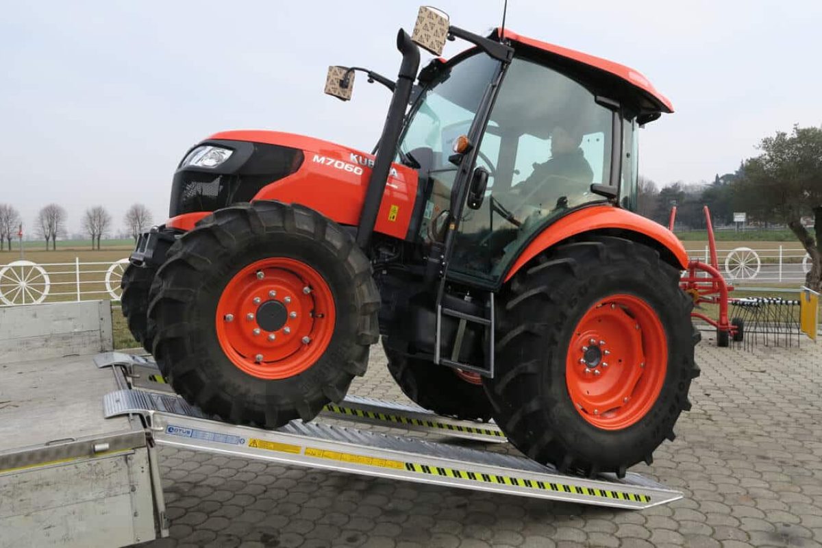 Trattore rosso su rampe di carico che sale sul camion